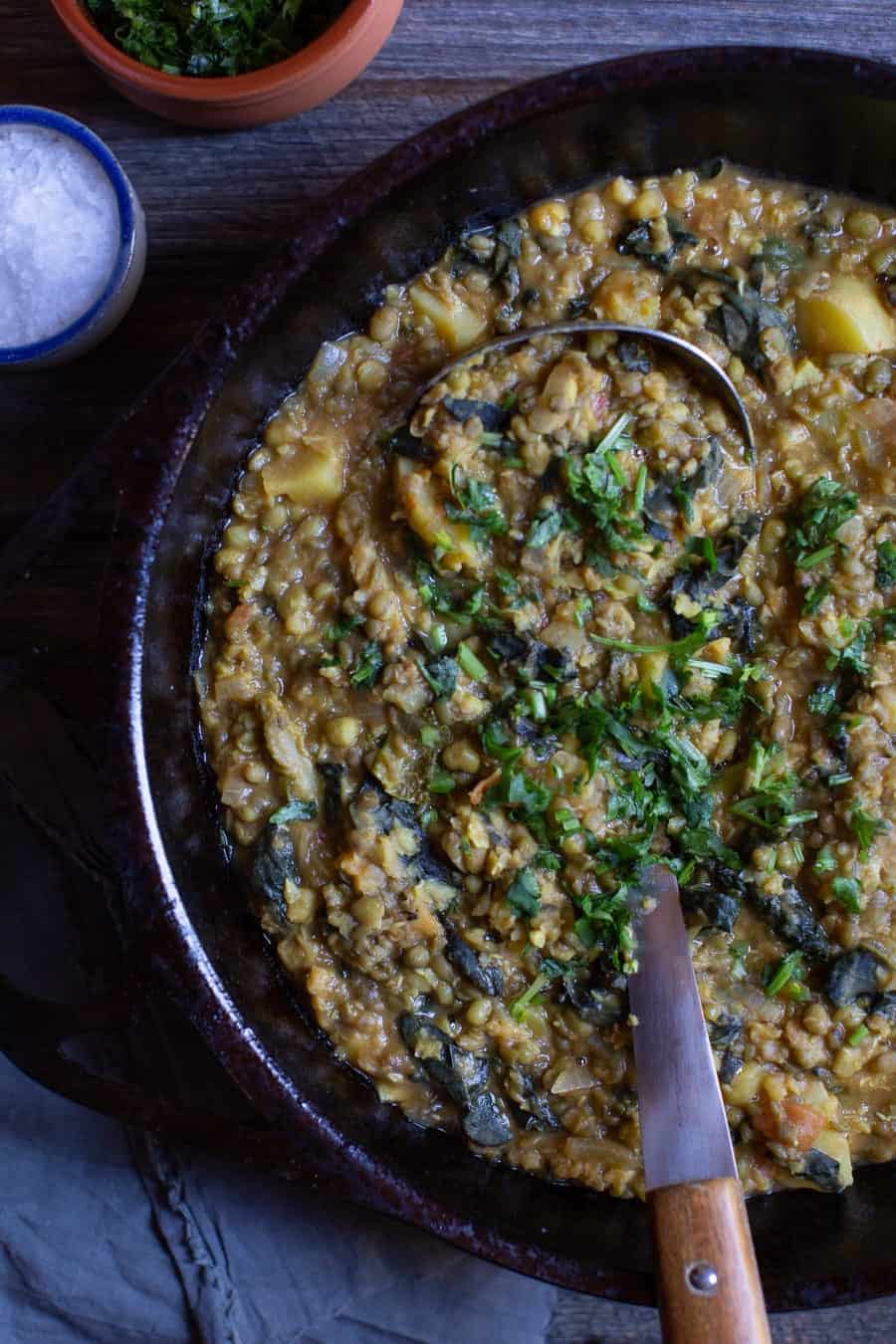 Hearty Mung Bean Stew With Kale in large pot with a ladle shot from above.