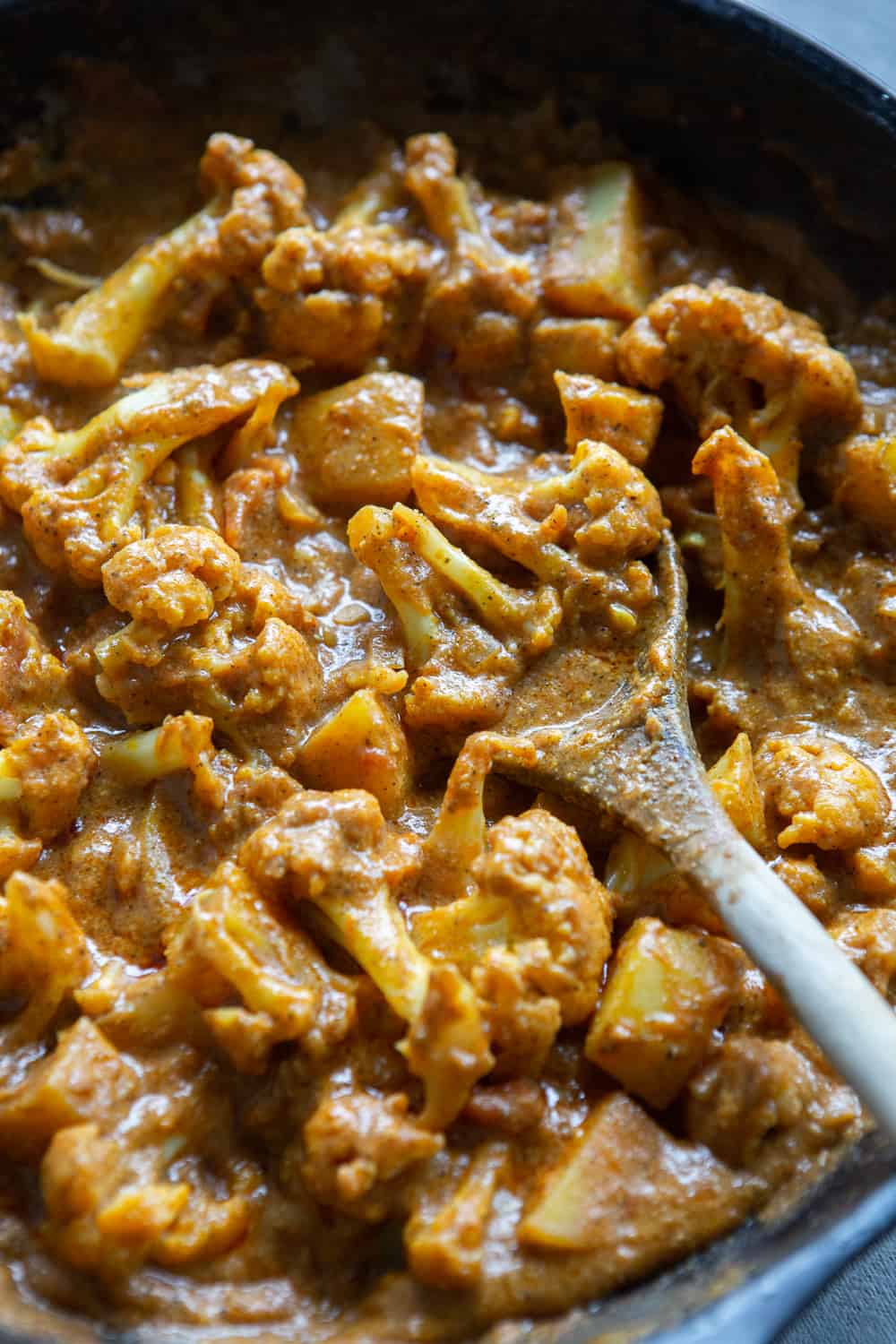 Cauliflower Potato Curry in cooking dish with wooden spoon