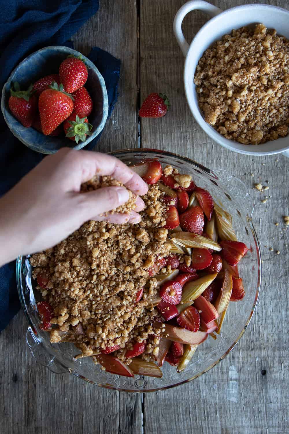Adding the crumble on top of strawberries and rhubarb.