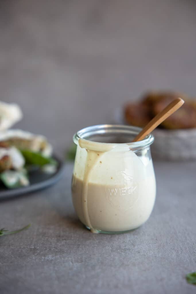Tahini dressing in a small jar with a spoon from the front.