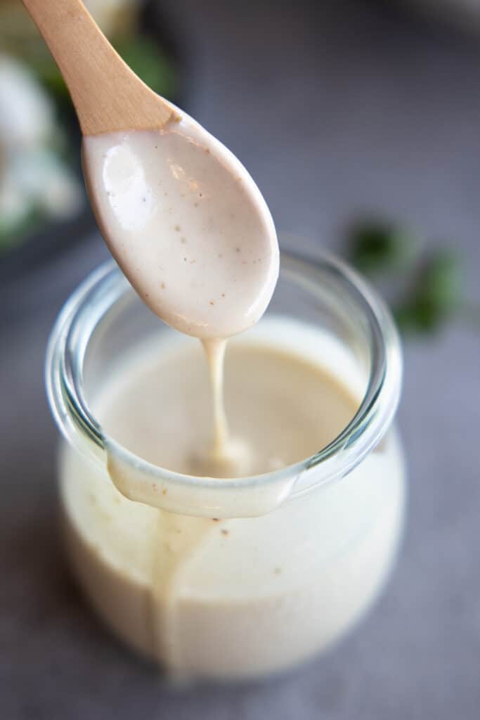 Tahini dressing in a small jar with a spoon dripping close up.