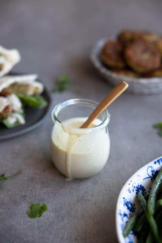 Tahini dressing in a small jar with a spoon.