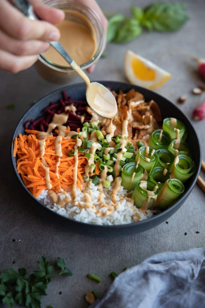 Tofu Buddha bowl with peanut sauce being drizzled over the top. 