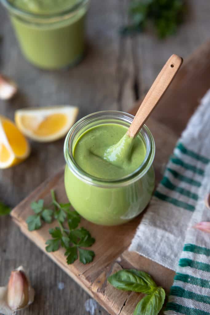 Green goddess sauce close up with small wooden spoon in jar.