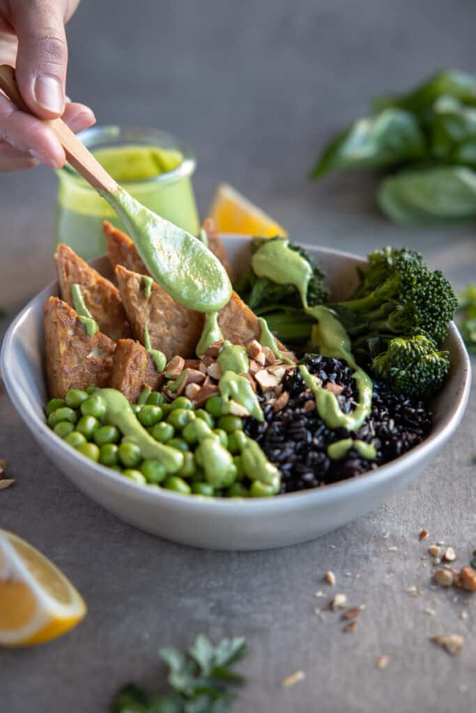 Tempeh buddha bowl with green goddess being drizzled over it.