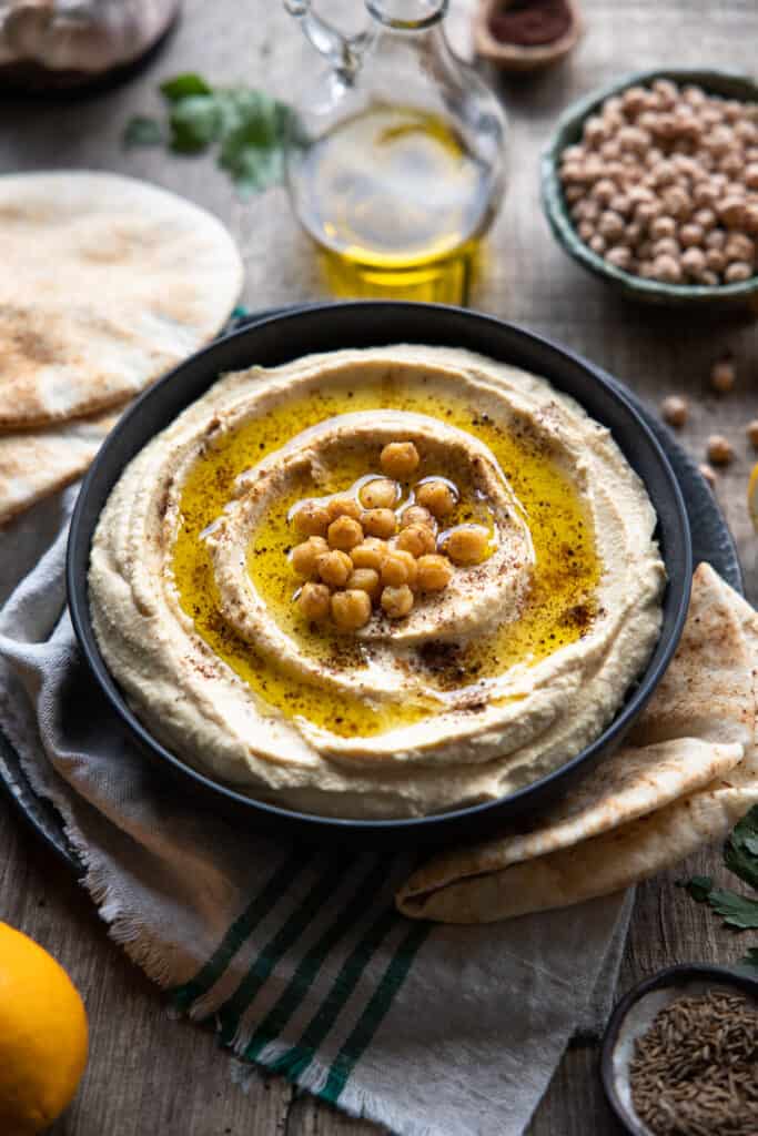 Hummus in a bowl with pita bread on the side, slightly further away at a 45-degree angle. 