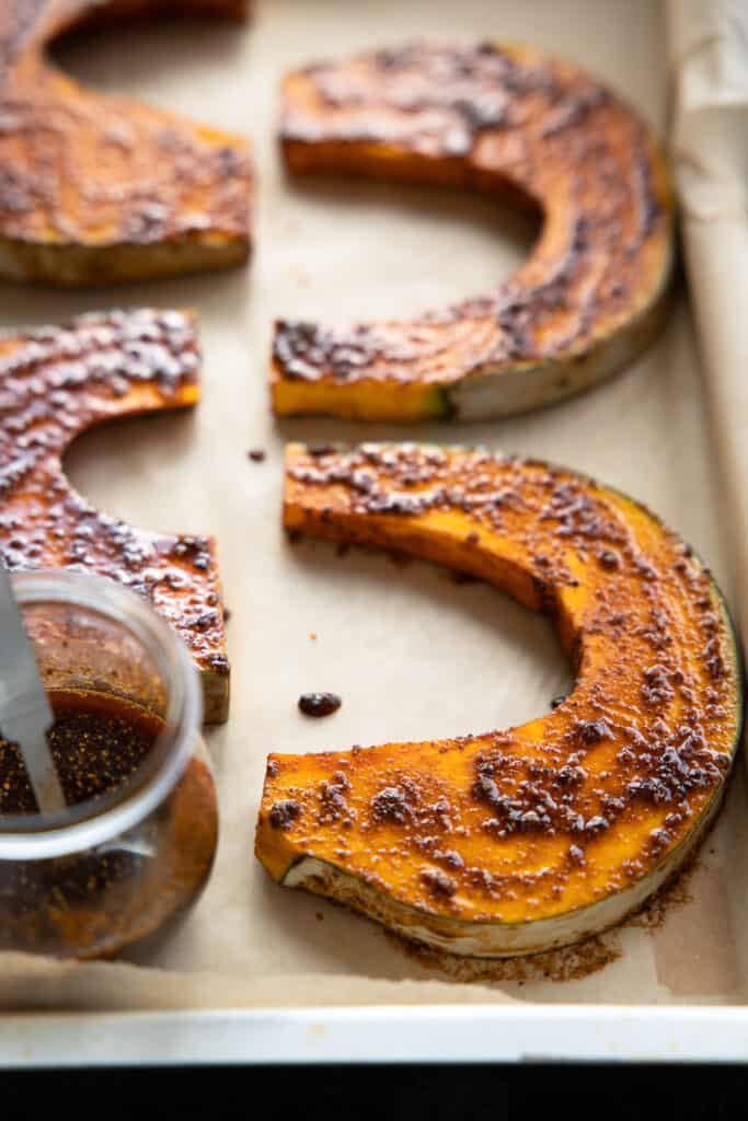 Raw pumpkin wedges on a baking sheet with spiced rubbed all over.