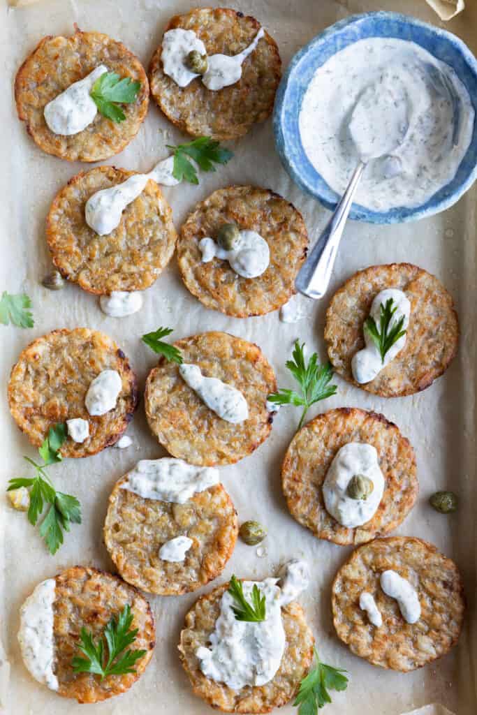 Crispy vegan hash browns on a baking tray with a caper mayo drizzled on top.