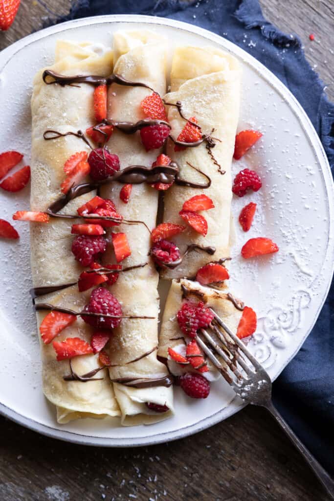 Rolled up crepes with filling of cream and topped with chocolate and berries.