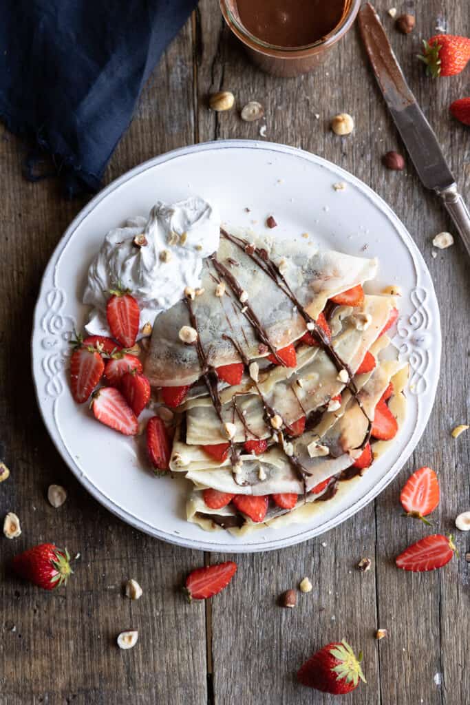 Crepes on a plate with chocolate hazelnut spread, coconut cream and strawberries.