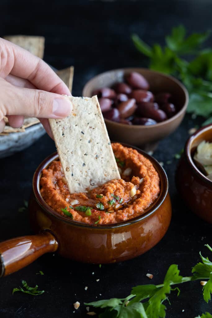 A cracker is dipped into chunky romesco dip.