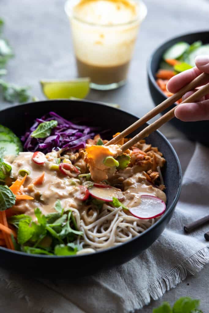 Using chopsticks to lift shredded tofu from the vegan noodle bowl.