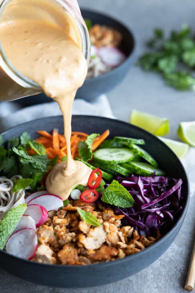 Pouring the peanut sauce over the vegan noodle bowl.