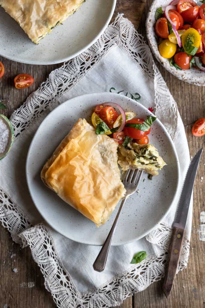 Vegan Spinach Pie with 'Ricotta' on plates with a tomato side salad. One bite has been taken from the pie.