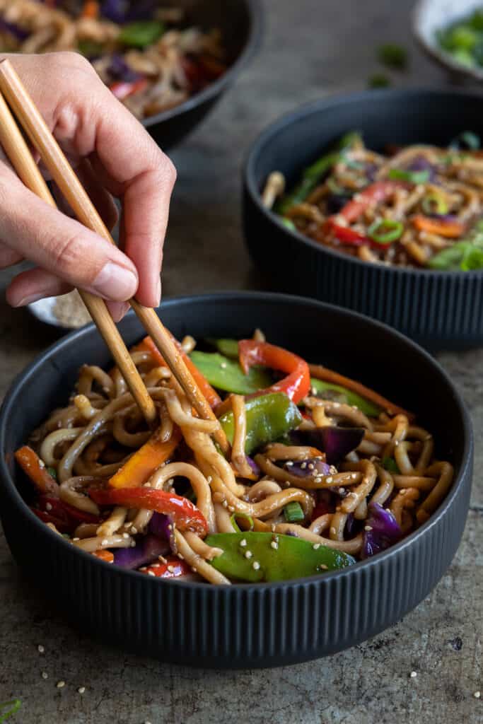 Vegan yaki udon in a bowl using chopsticks.