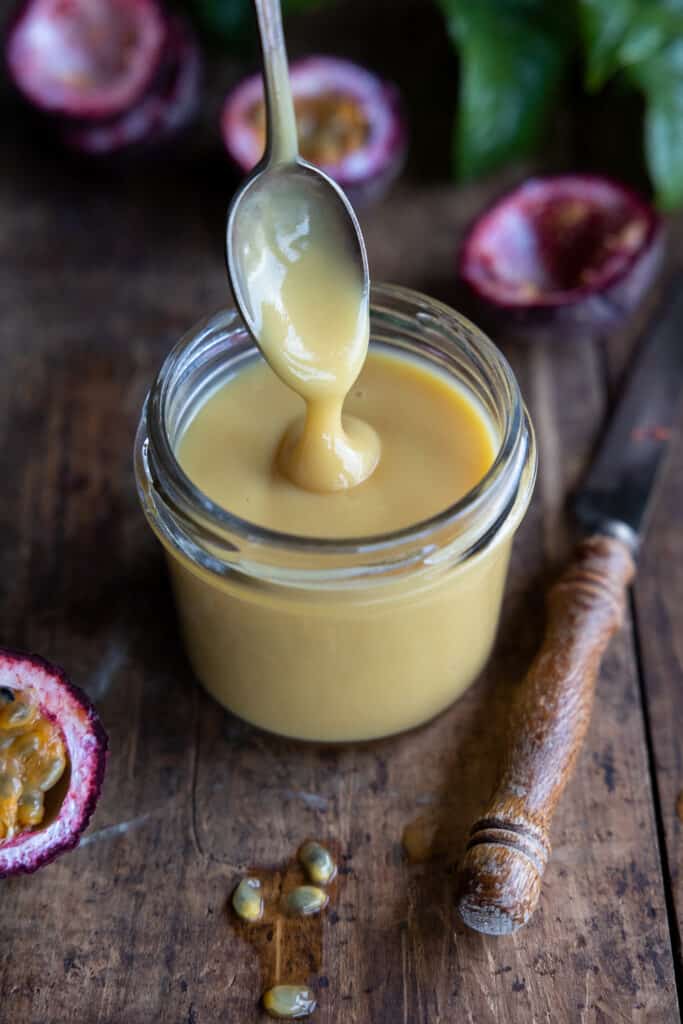 Vegan passionfruit curd with a spoon in a jar.