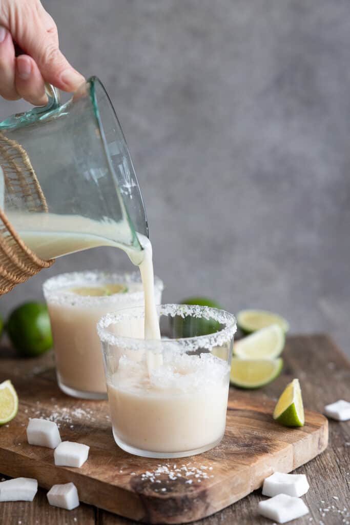 Pouring Creamy Coconut, Lime & Lychee Mocktail into glasses.