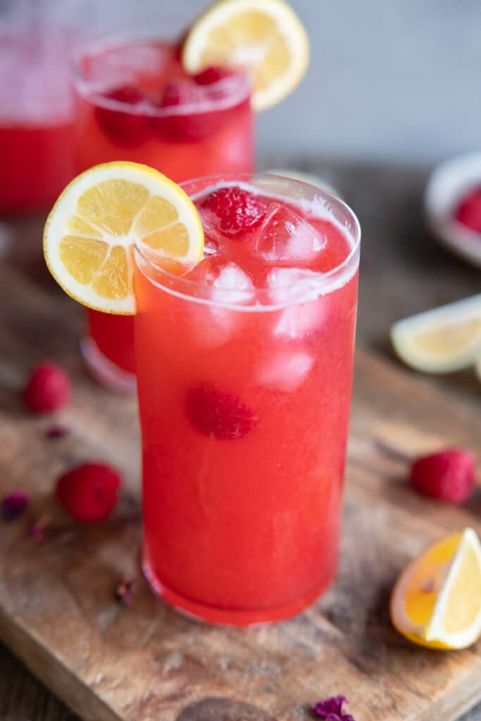 Close up of the raspberry rose lemonade in a glass with ice, fresh raspberries and a lemon slice.