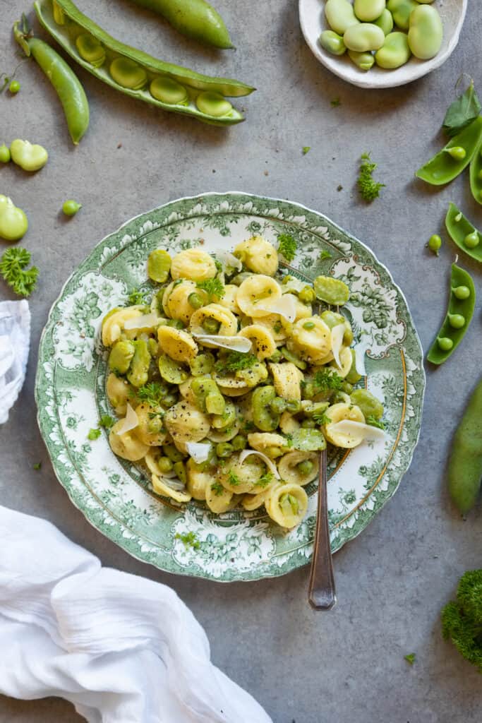 Broad bean pasta with peas on a green plate.